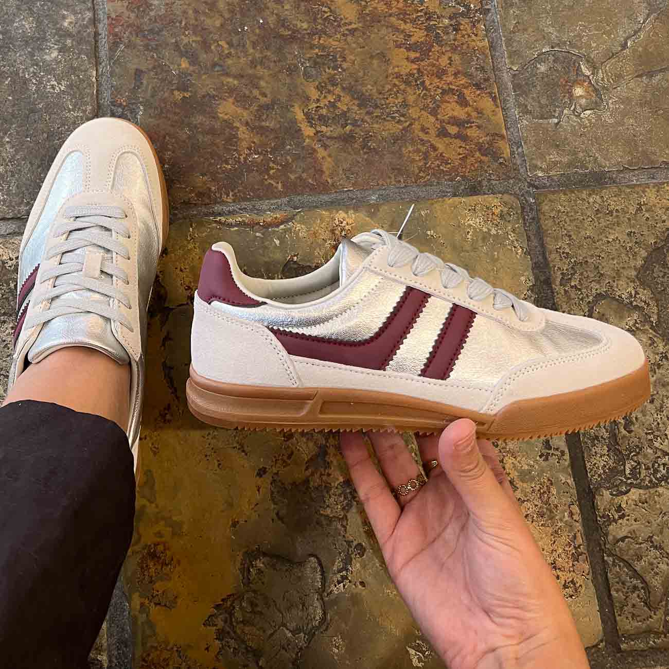 White and burgundy sneakers with brown soles on a stone floor