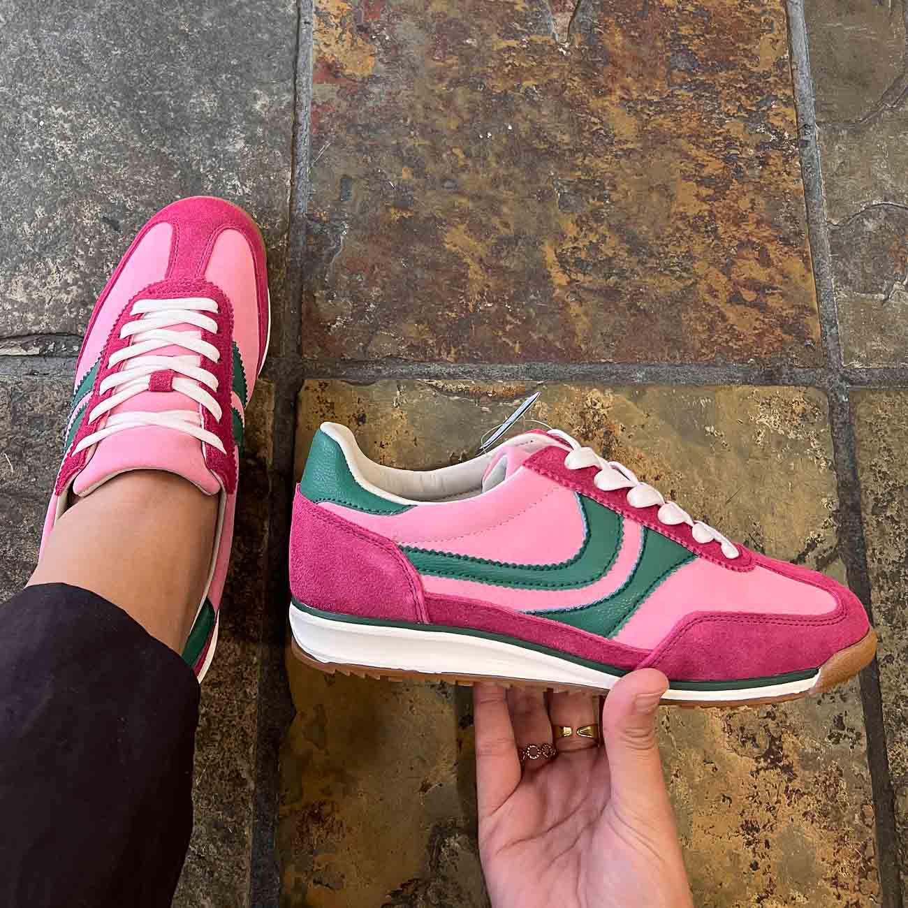 Pink and green sneakers with a brand logo on a textured floor.