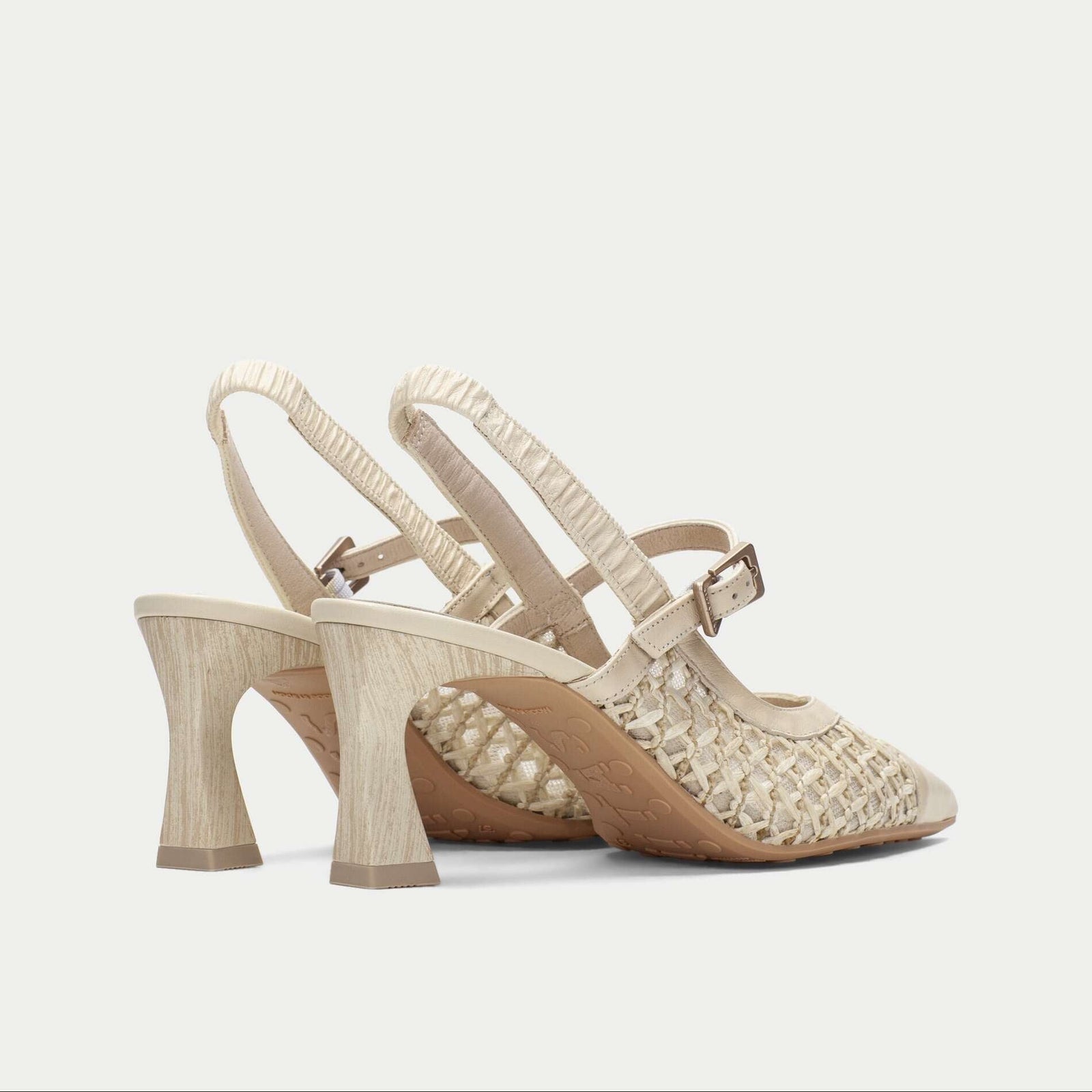 Pair of beige high-heeled shoes with embellishments on a light gray background