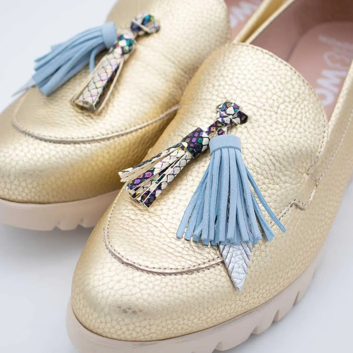 Gold loafers with blue tassels on a white background