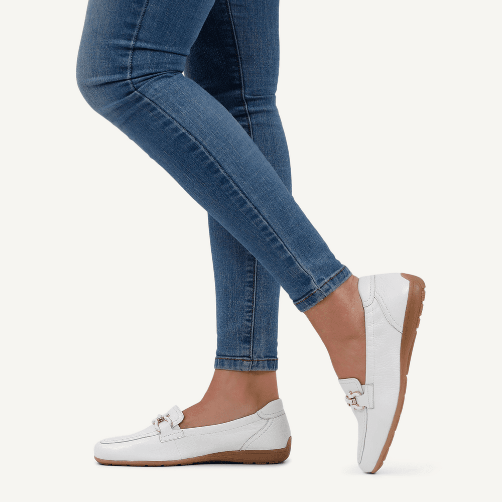 Person wearing blue jeans and white loafers on a light gray background