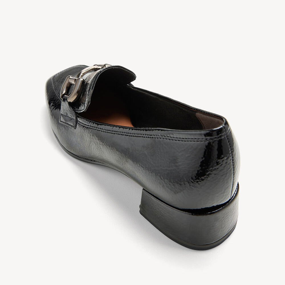 Black patent leather loafer with a buckle on a white background