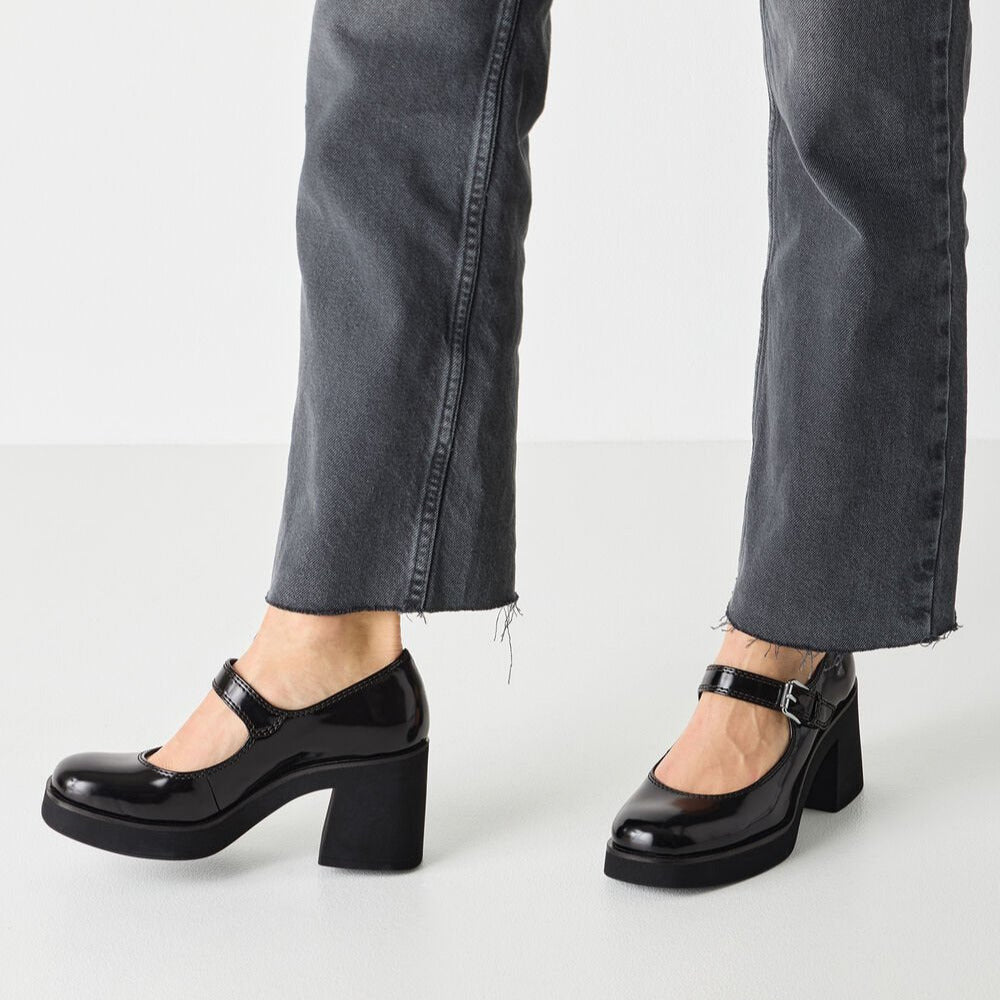 Black platform shoes worn with gray jeans on a white background
