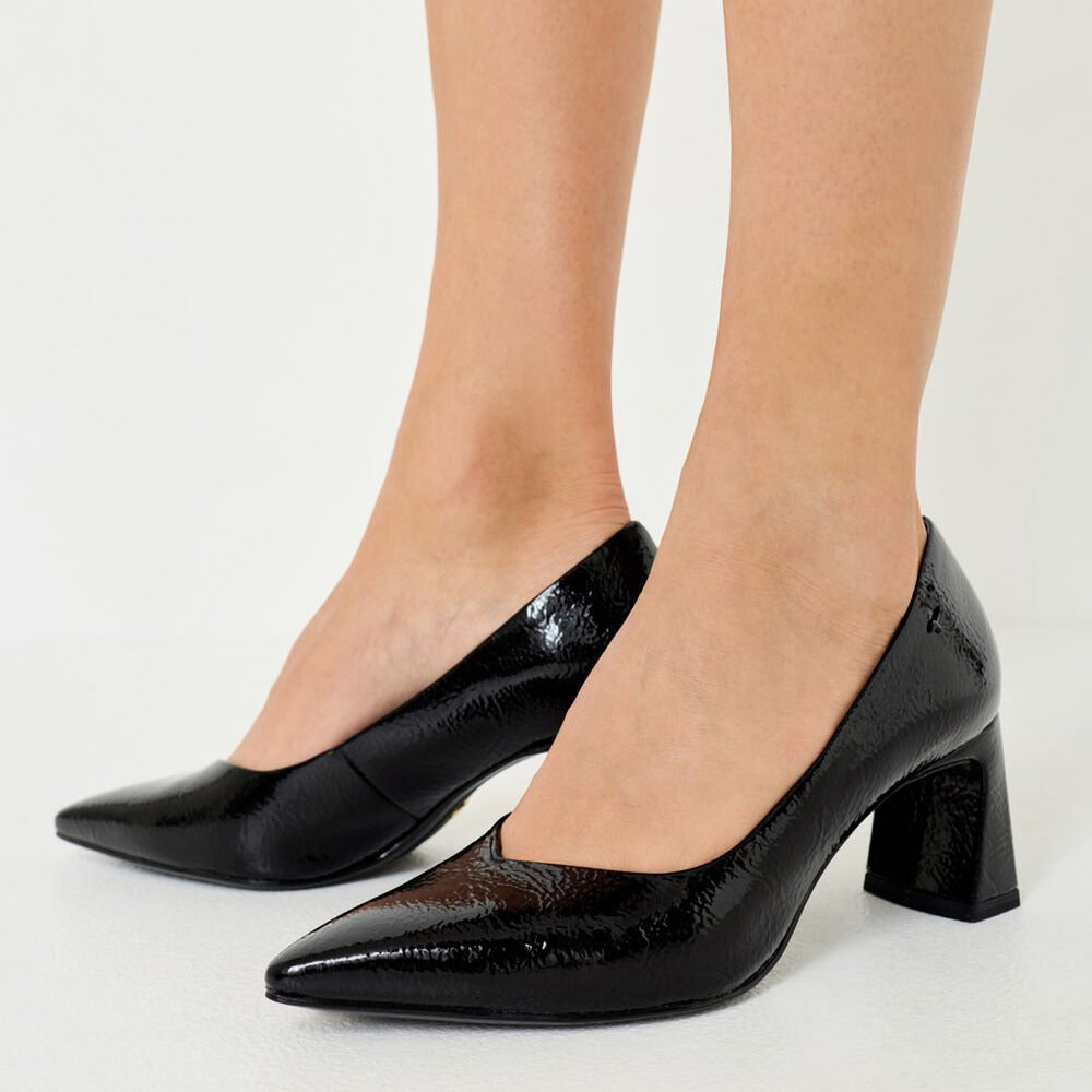 Black patent leather shoes worn by a person on a light gray background