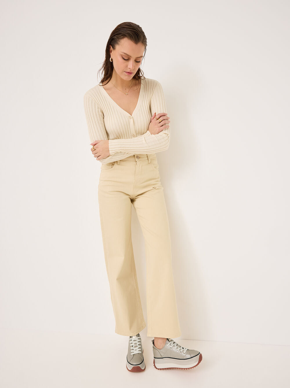 Woman wearing a beige ribbed sweater and pants with gray shoes on a white background