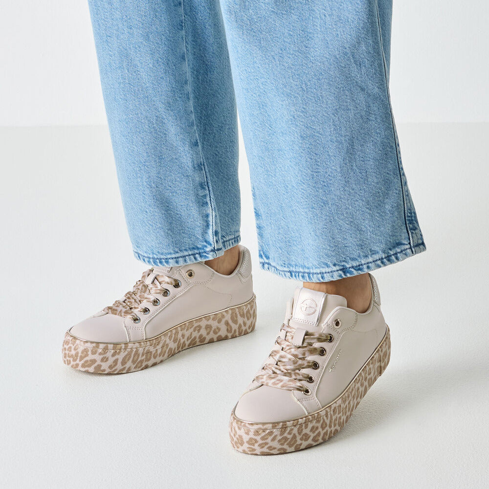 White sneakers with leopard print soles worn with light blue jeans on a white background