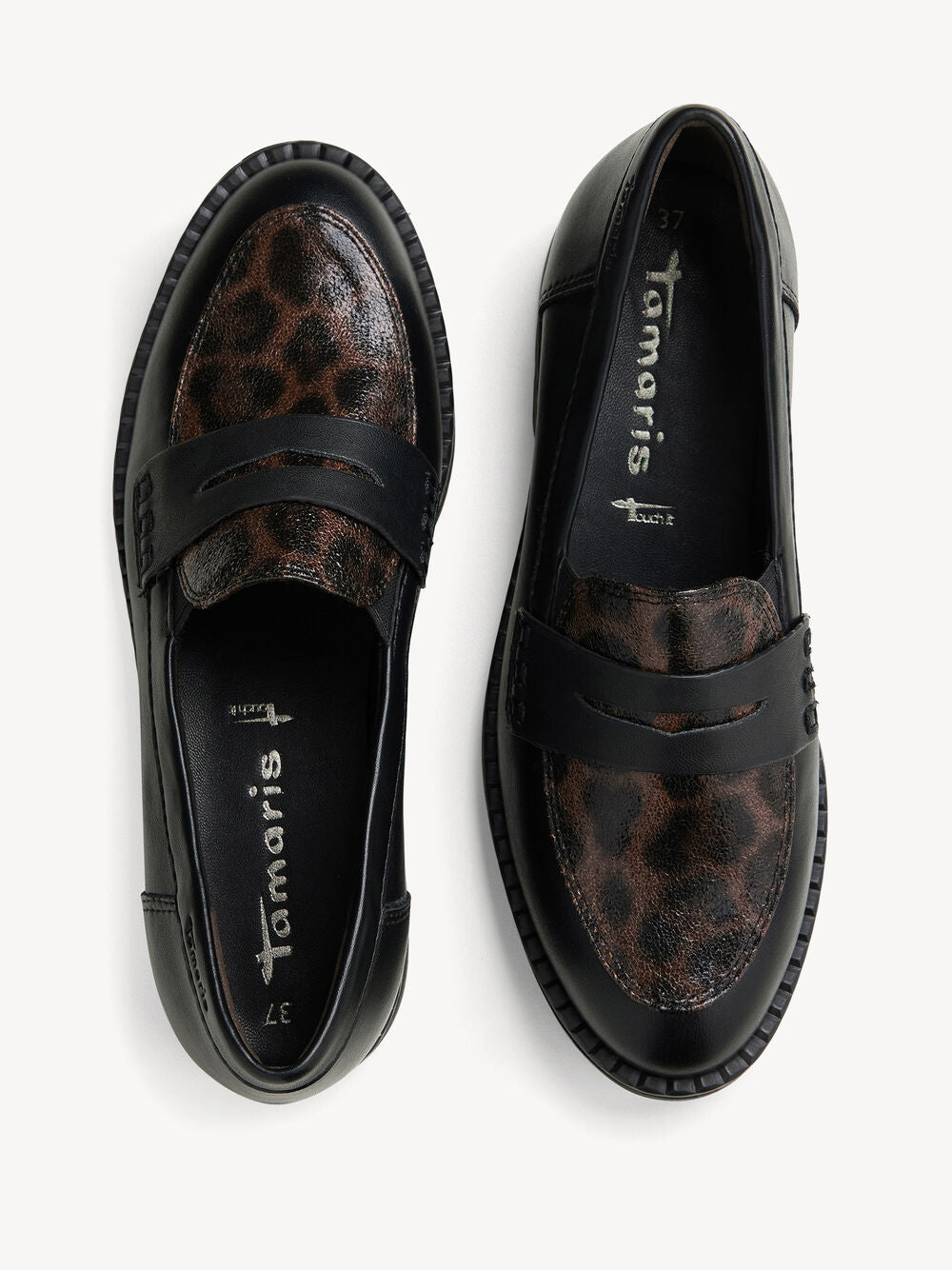 A pair of black leather penny loafers with brown and black leopard print panels, shown from a top-down view on a light gray background. The brand name 'Tamaris' is visible on the insoles.