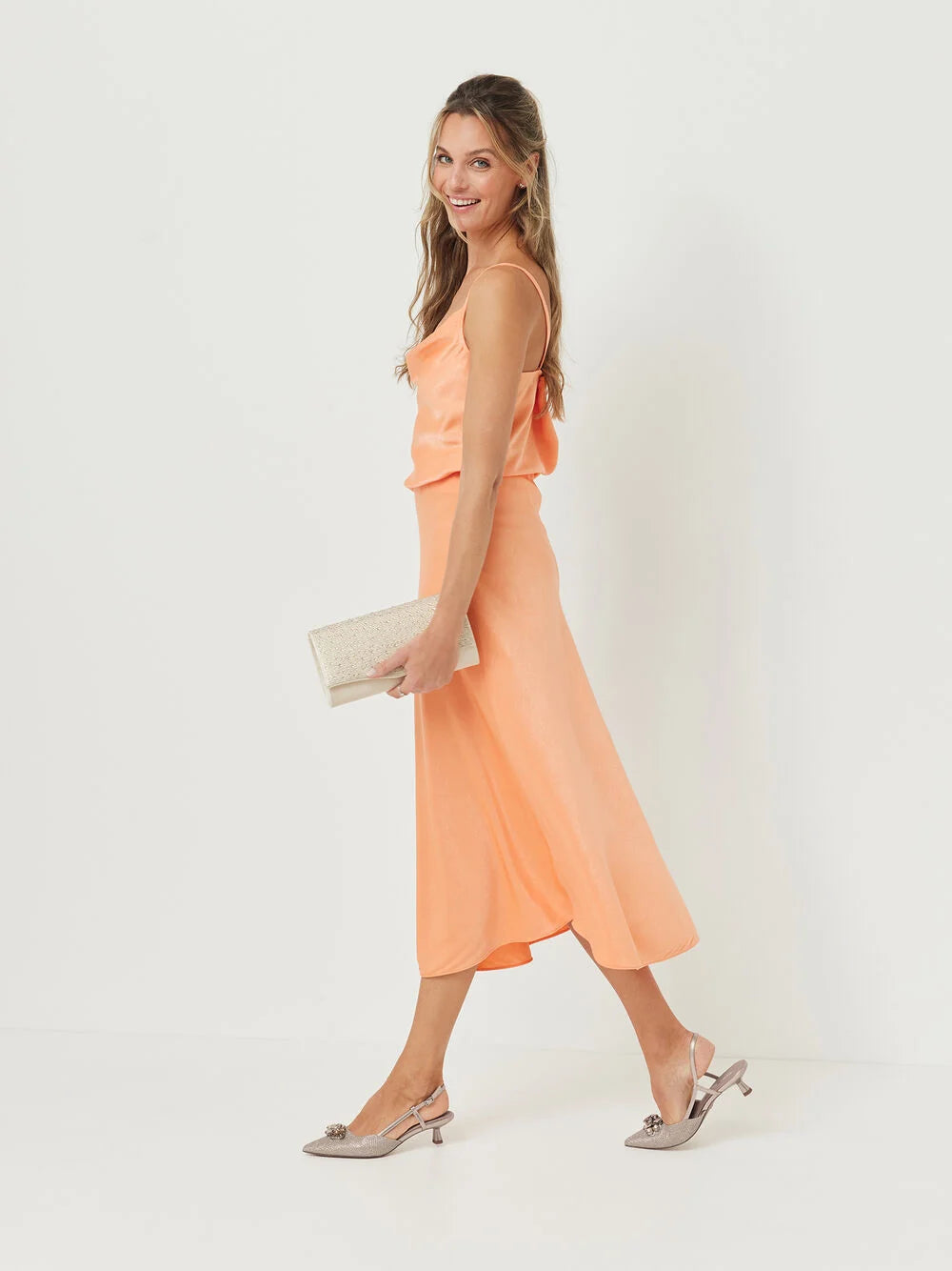 Woman wearing a peach dress holding a clutch against a white background