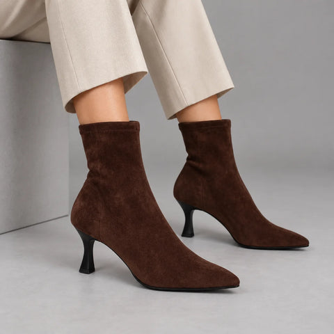 Model wearing Miss Elastic Zeta brown stretch ankle boots with ivory cropped trousers, seated in a grey studio
