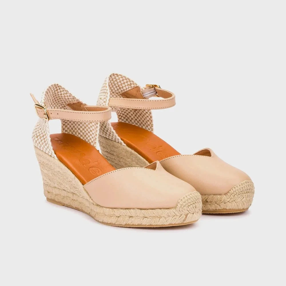 Pair of beige wedge sandals with woven details on a light gray background