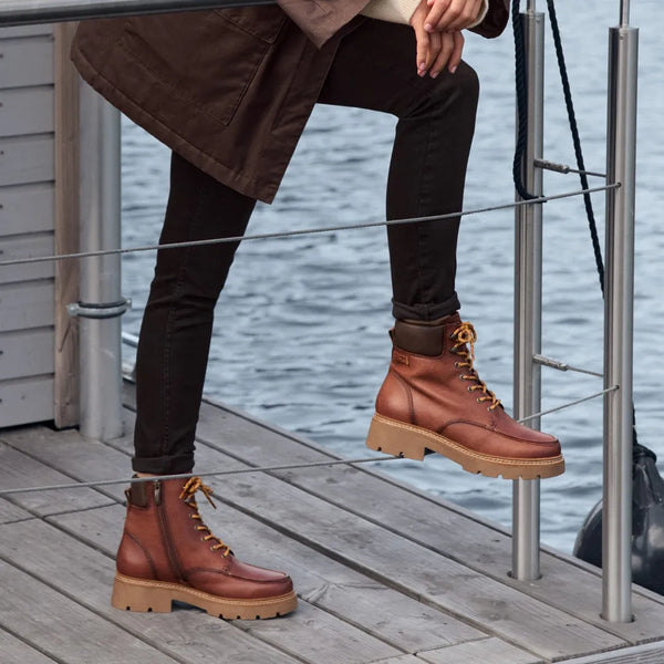 Woman wearing waterprood boots by a railing at the lake.