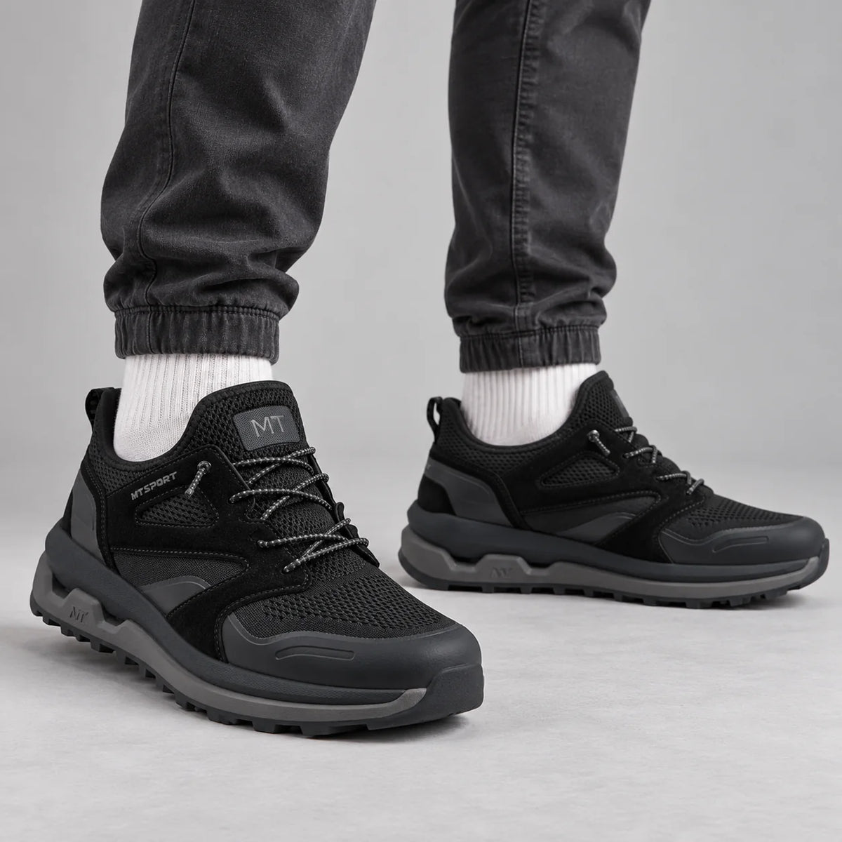 Marco Tozzi men's black MT Sport chunky trainers worn with graphite joggers and off-white socks in a grey studio.