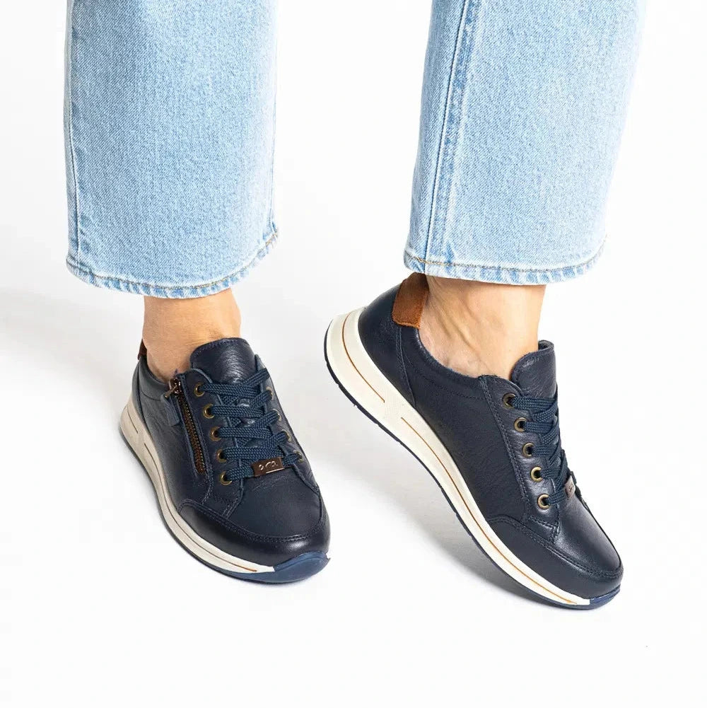 A person wearing light blue jeans and navy low-top sneakers with cream midsoles, shown from the calves down against a clean white background.