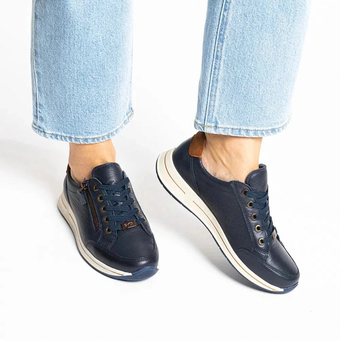 A person wearing light blue jeans and navy low-top sneakers with cream midsoles, shown from the calves down against a clean white background.