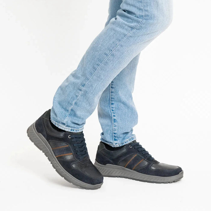 Person wearing navy shoes with brown stripes and light blue jeans on a white background