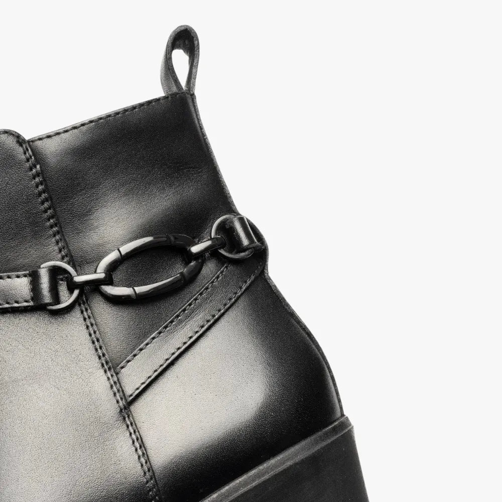 Close-up of a black leather boot with a chain detail on a white background