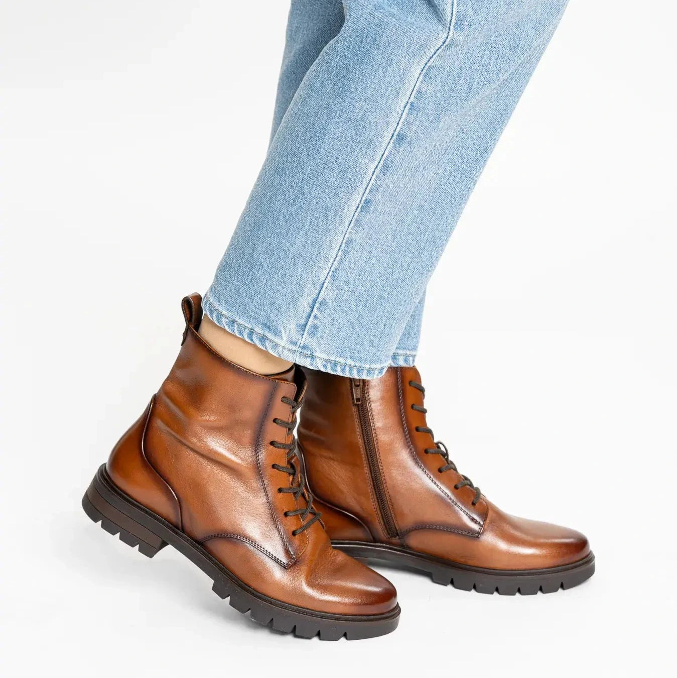 Brown leather boots worn with light blue jeans on a white background
