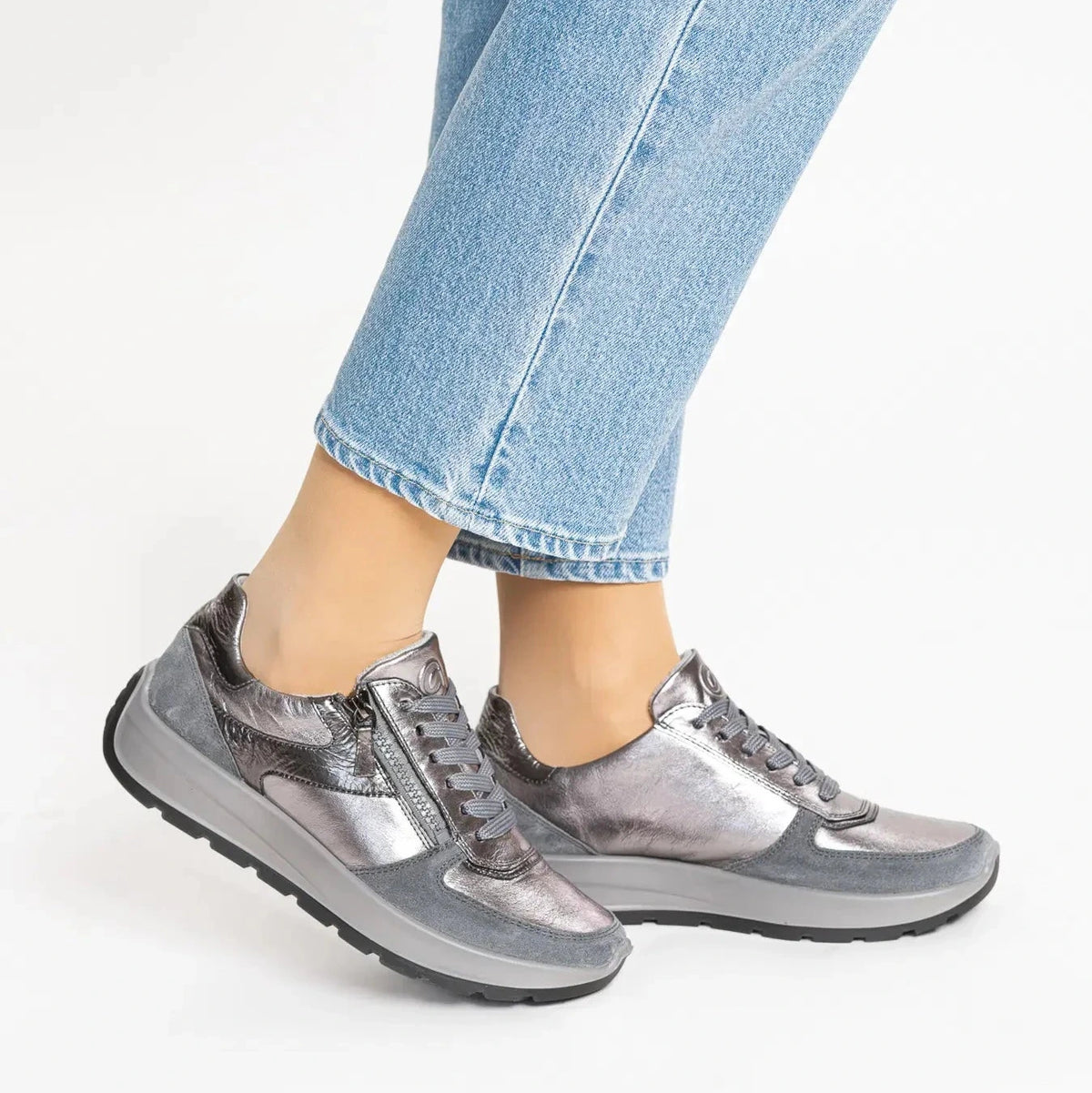 A person wearing metallic gray low-top sneakers with light blue cropped jeans, shown from the calves down against a clean white studio background.