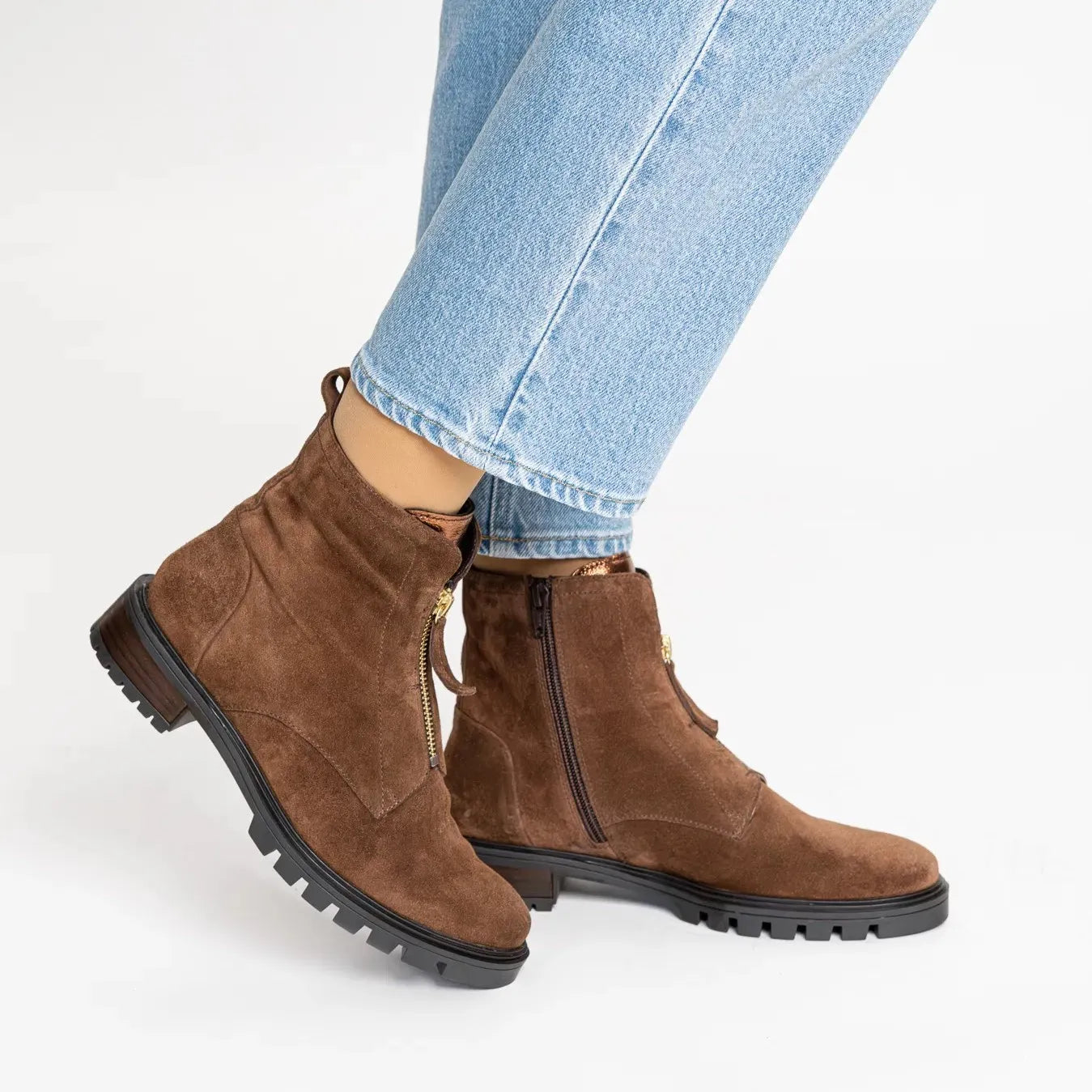 Brown suede ankle boots worn with light blue jeans on a white background