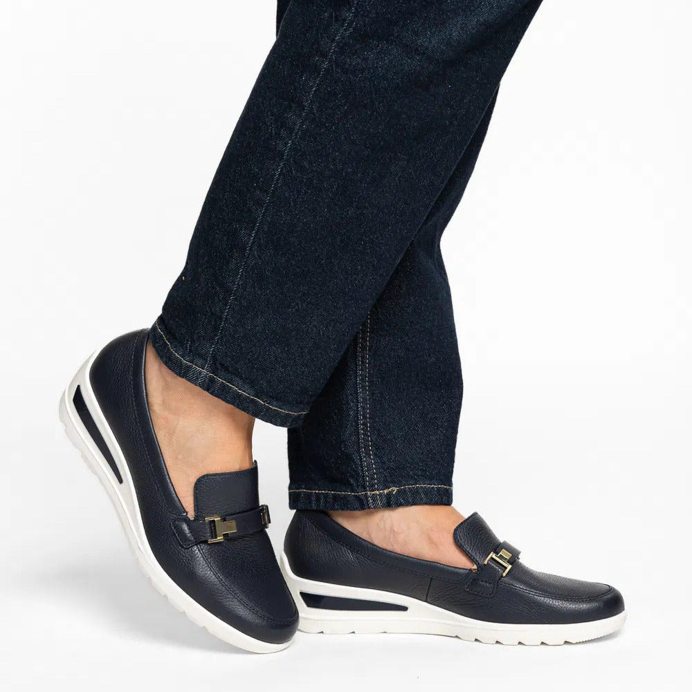 Person wearing navy loafers with white soles and dark jeans on a white background