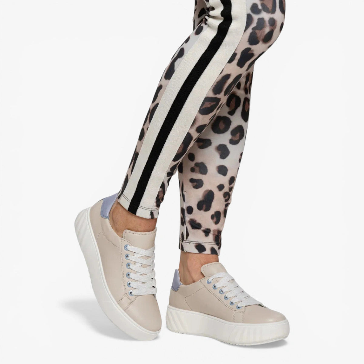 Leopard print leggings with white and black stripes worn with beige sneakers on a white background