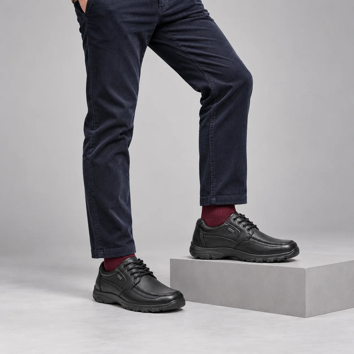 G-Comfort A-7825 men's black leather lace-up shoes styled with navy corduroys and burgundy socks in a grey studio.