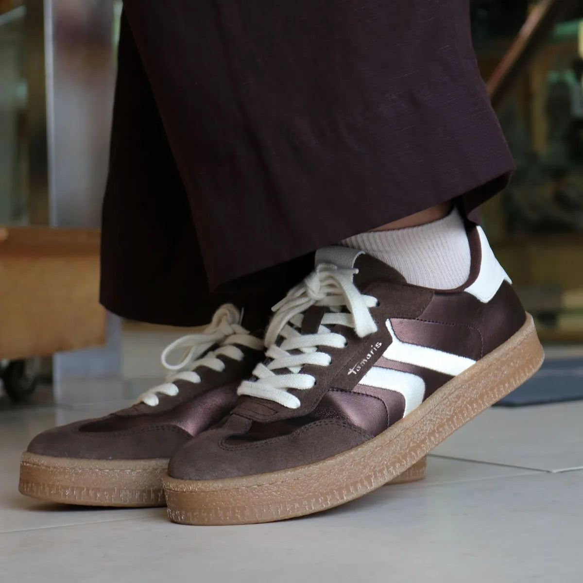 Brown sneakers with white laces and soles worn indoors.