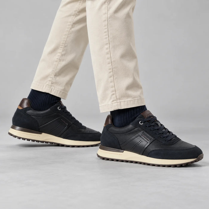 Marco Tozzi men's navy MT Sport trainers styled with ecru trousers and navy socks in a neutral grey studio.
