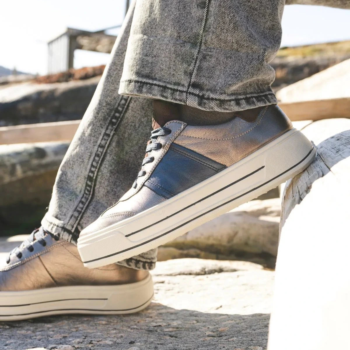 Person wearing brown sneakers with white soles on a rocky surface.