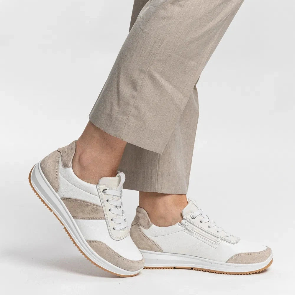 White sneakers with brown soles worn with beige pants on a white background