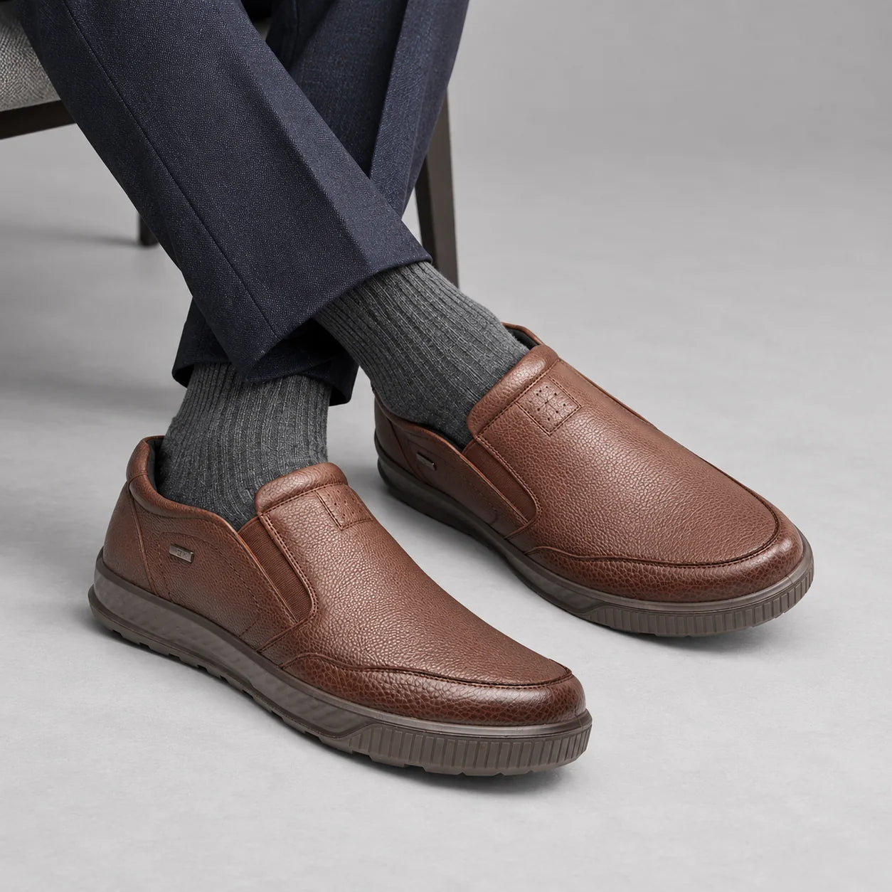 G-Comfort A-951 men's tan leather slip-on shoes styled with navy trousers and grey socks in a neutral studio.