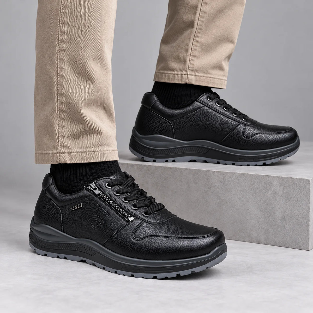 G-Comfort R-1282 men's black lace and zip trainers worn with stone trousers and black socks in a grey studio.