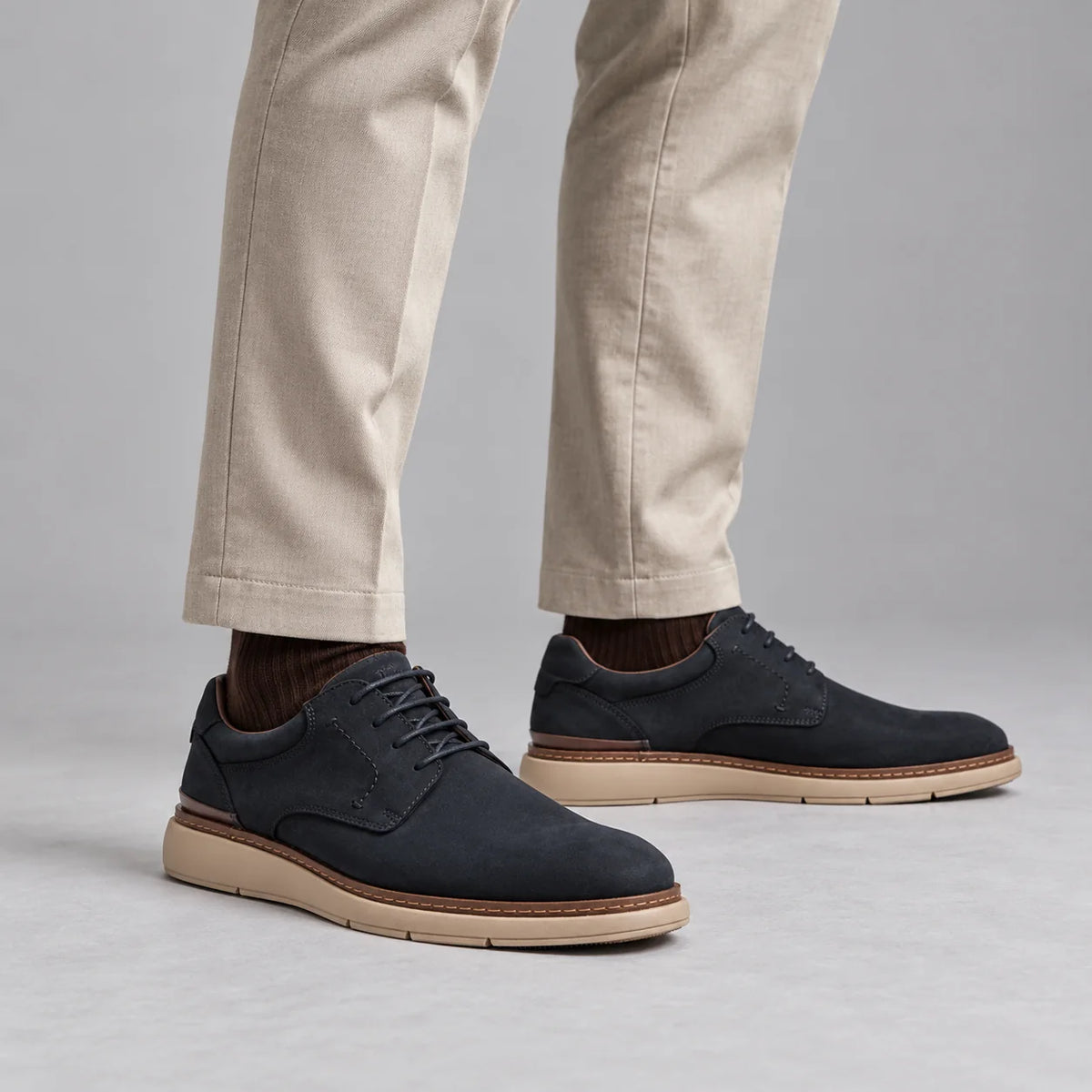 Tamaris men's navy leather lace-up shoes worn with stone pleated trousers and brown socks in a neutral studio.