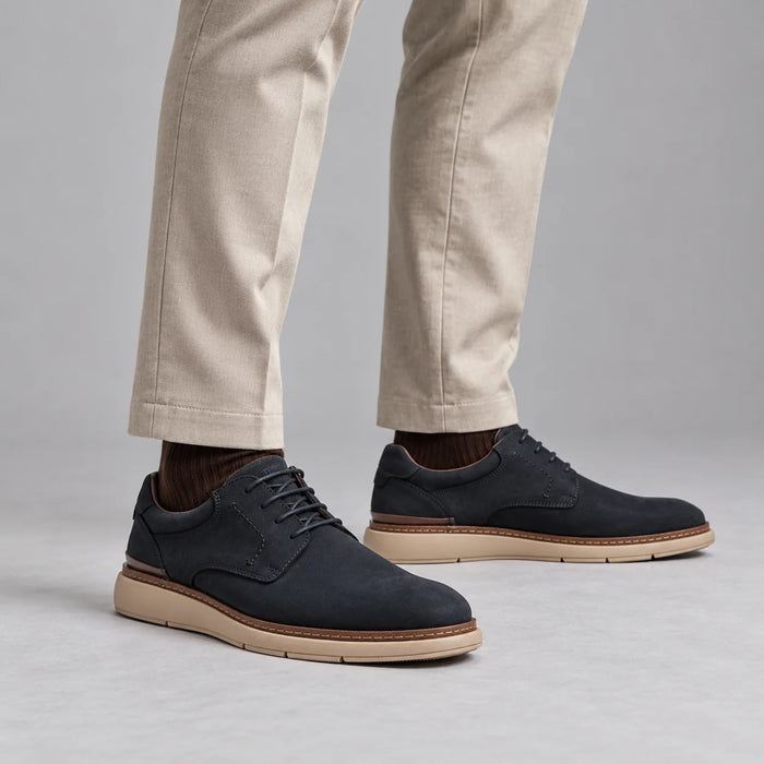 Tamaris men's navy leather lace-up shoes worn with stone pleated trousers and brown socks in a neutral studio.
