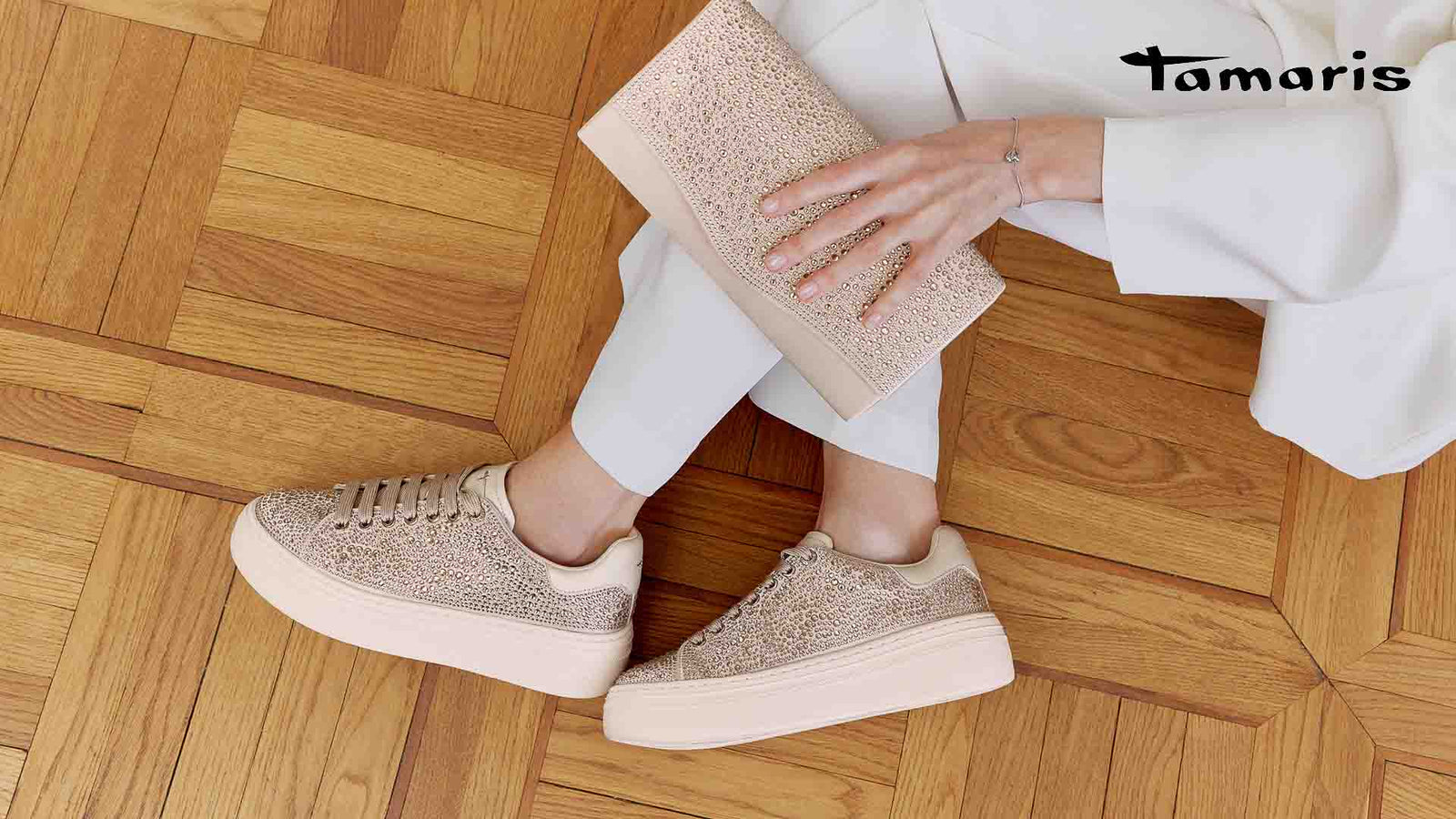 Person wearing sparkly sneakers on a wooden floor with Tamaris branding.