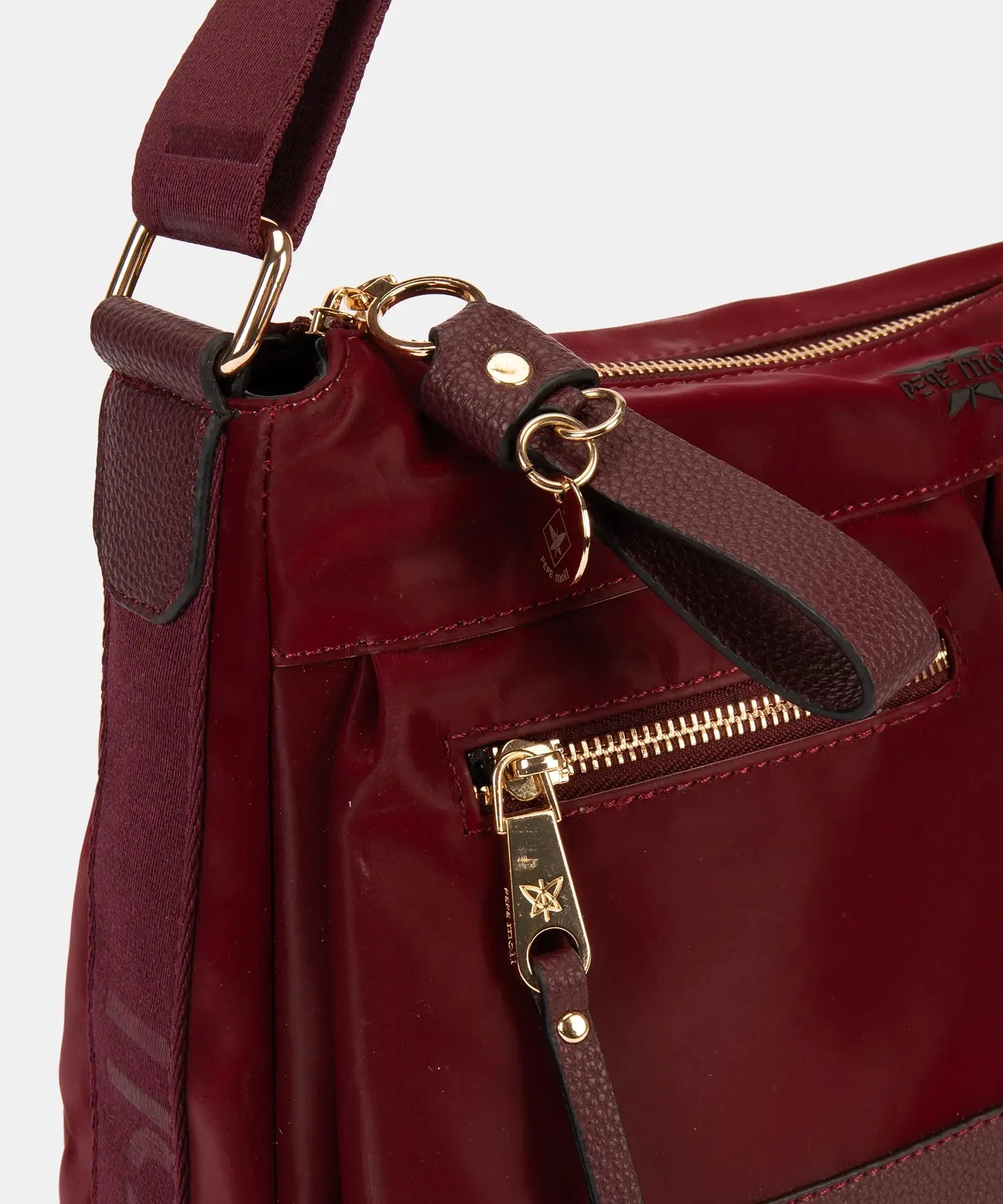 Close-up of a maroon handbag with gold zippers and hardware on a white background