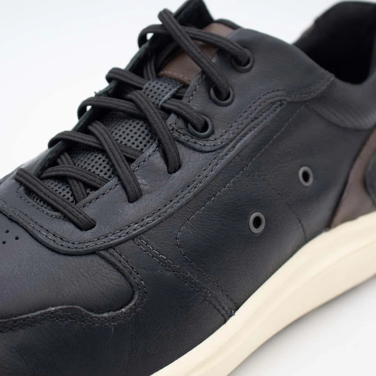 Black leather sneaker with a white sole on a light grey background