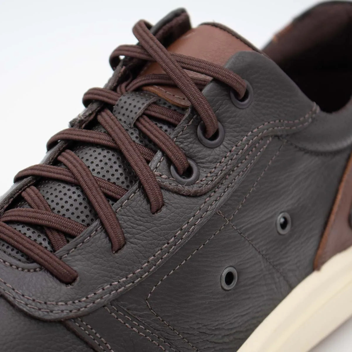 Close-up of a brown leather sneaker with brown laces on a light gray background