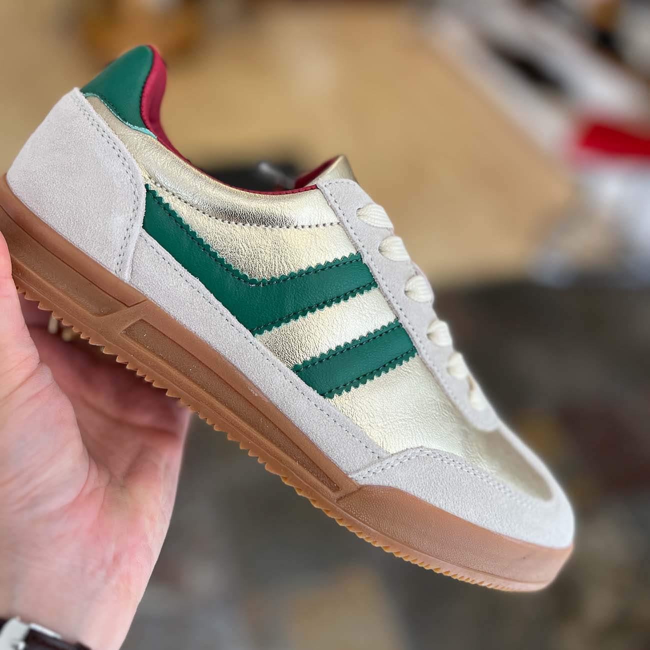 White sneaker with green stripes held by a hand against a blurred background