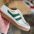 White sneaker with green stripes held by a hand against a blurred background