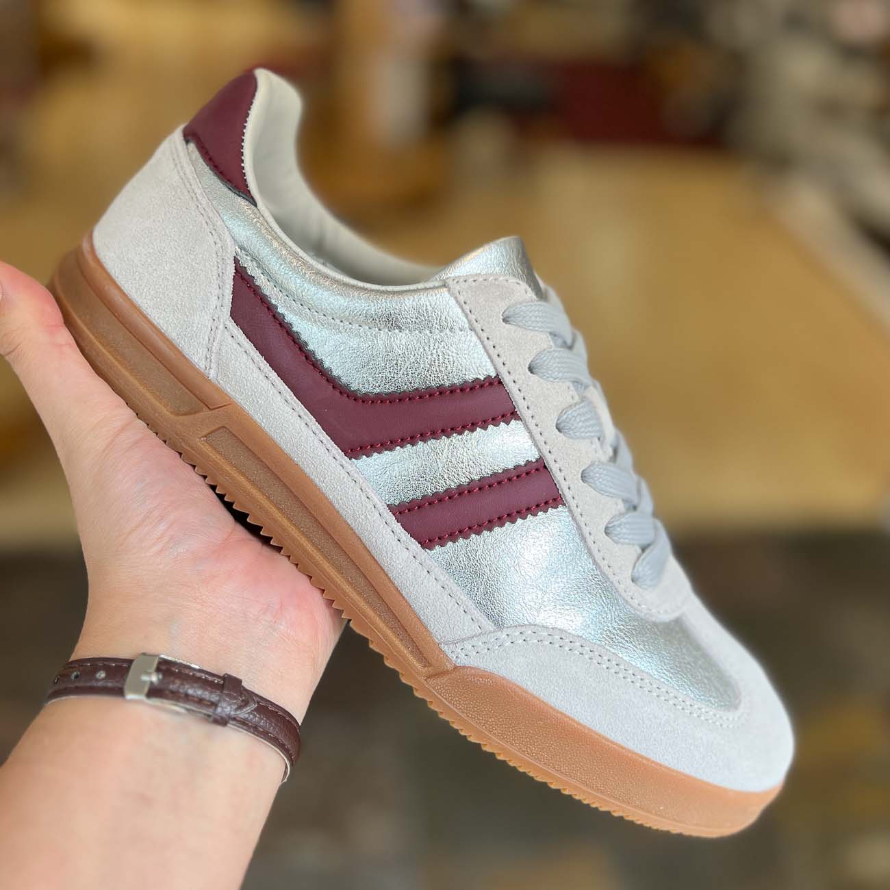 White sneaker with maroon stripes held by a hand against a blurred background