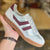 White sneaker with maroon stripes held by a hand against a blurred background