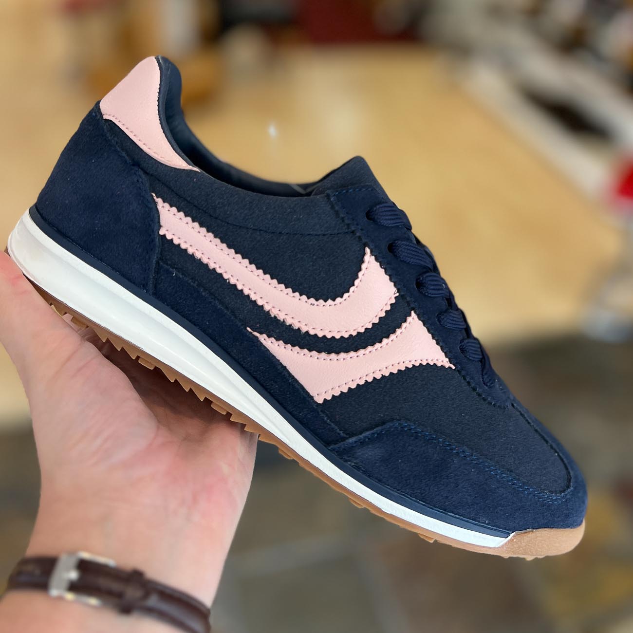 Navy blue sneaker with pink swoosh held by a hand against a blurred background