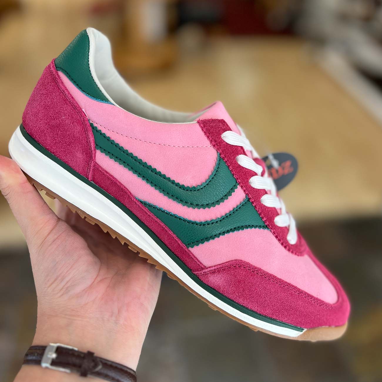 Pink and green sneaker held in a hand with a blurred background
