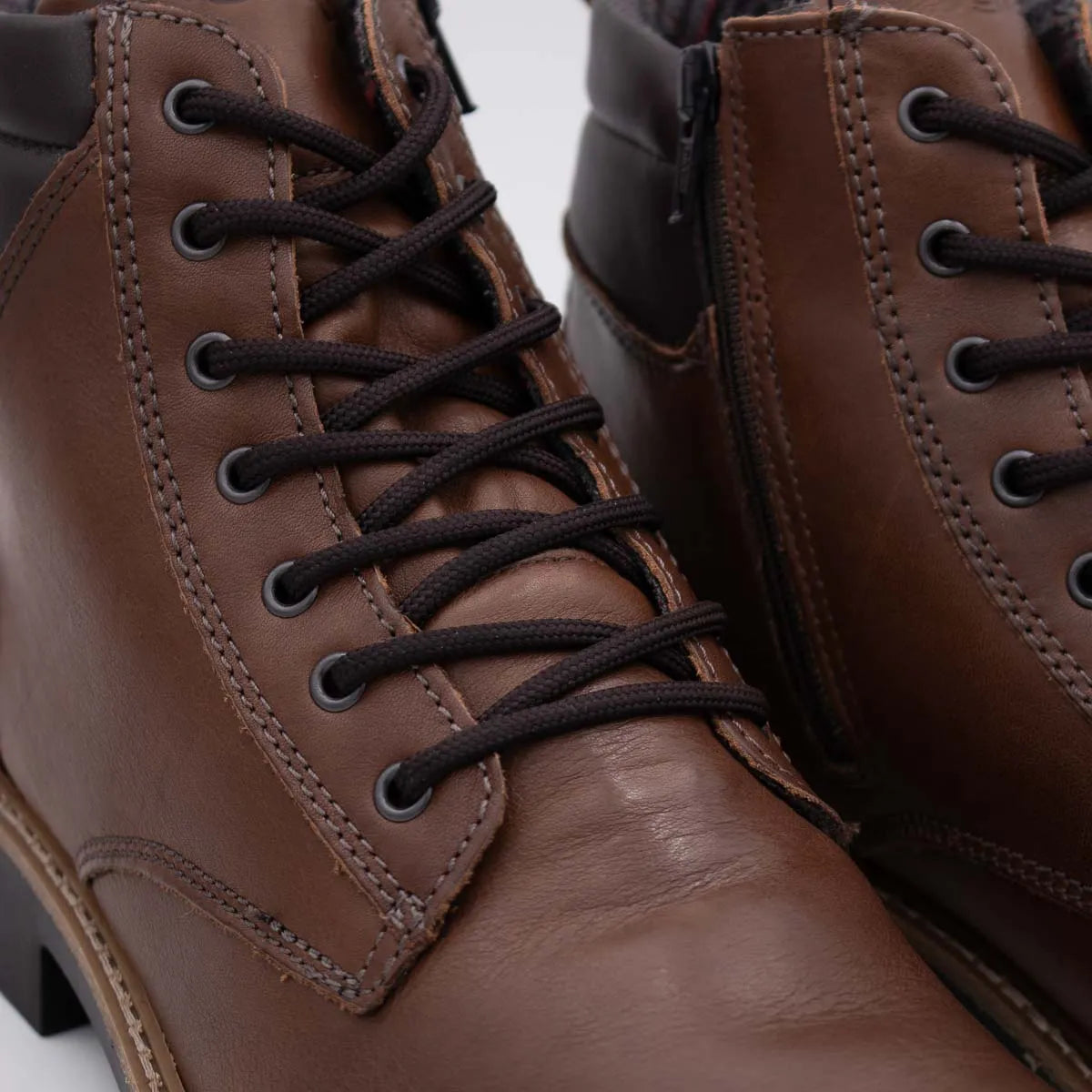Close-up of brown leather boots with black laces on a light gray background