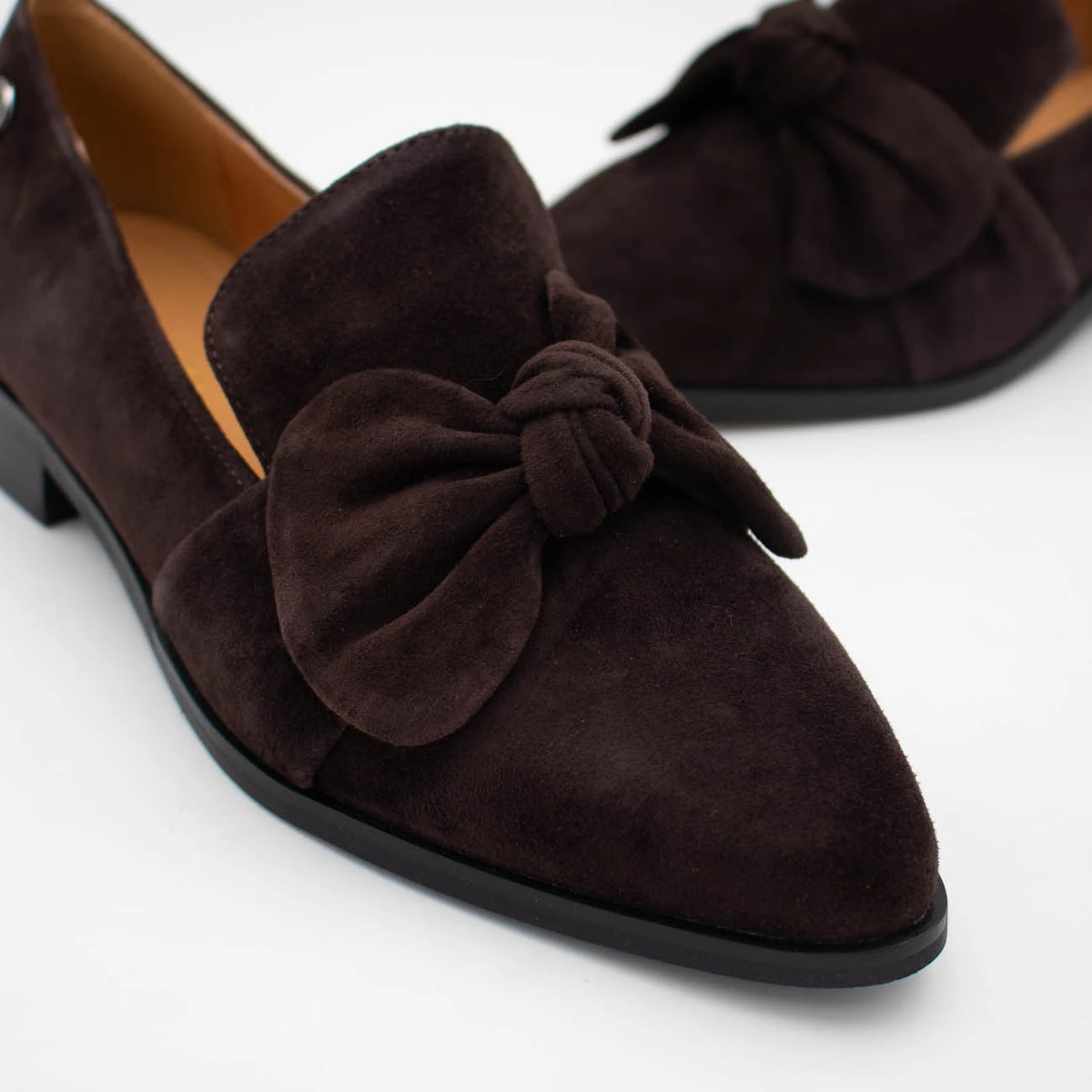 A pair of dark brown suede pointed-toe flats with large knotted bow details on the vamp, shown on a clean white background.