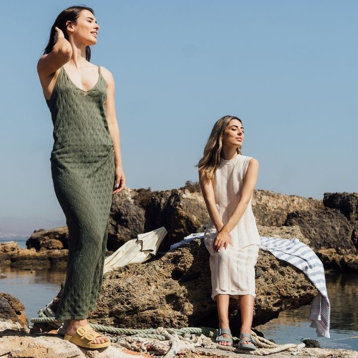 Two women standing on rocky coastal terrain with a clear blue sky.