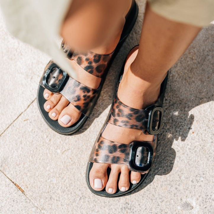 Leopard print sandals with black straps worn on a light surface
