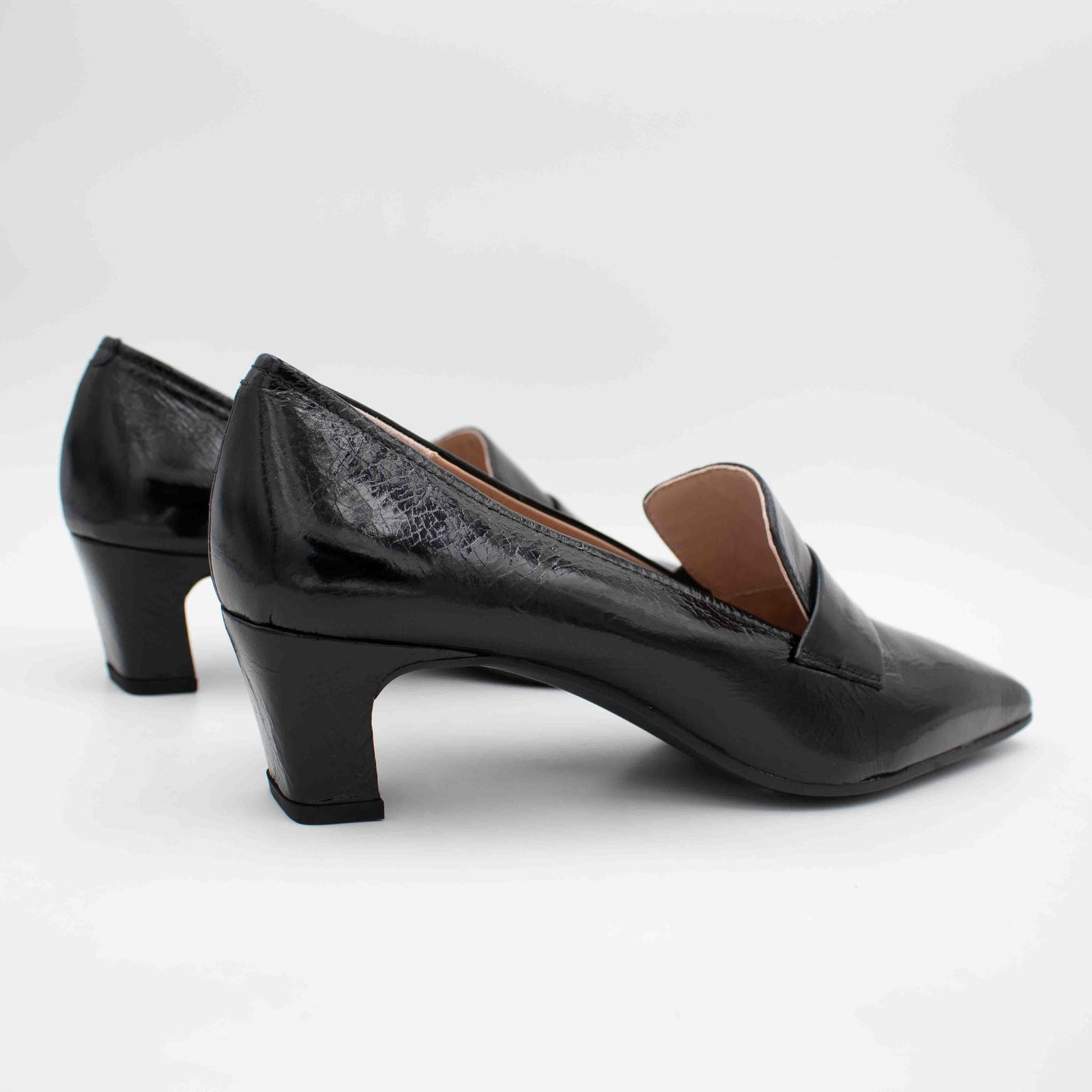 A pair of black pointed-toe heeled pumps with a glossy finish, shown from a side profile view on a light gray background.