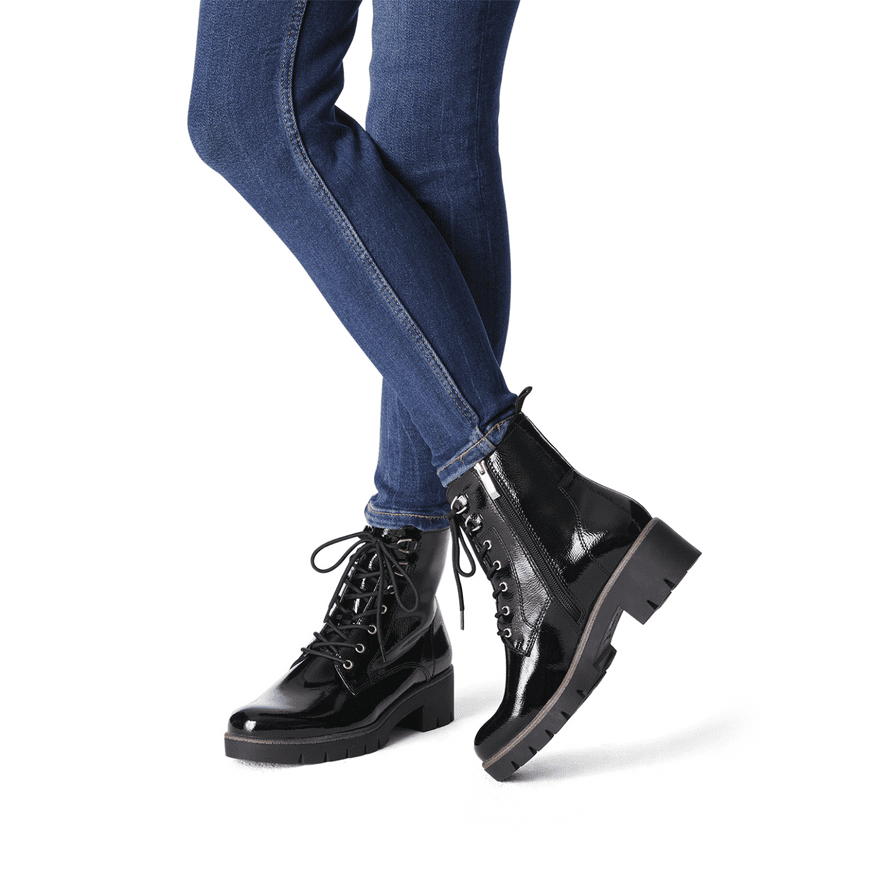 A fashionable woman showcasing the black patent ankle boots with blue jeans.